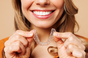 Woman in orange shirt about to put in Invisalign aligner